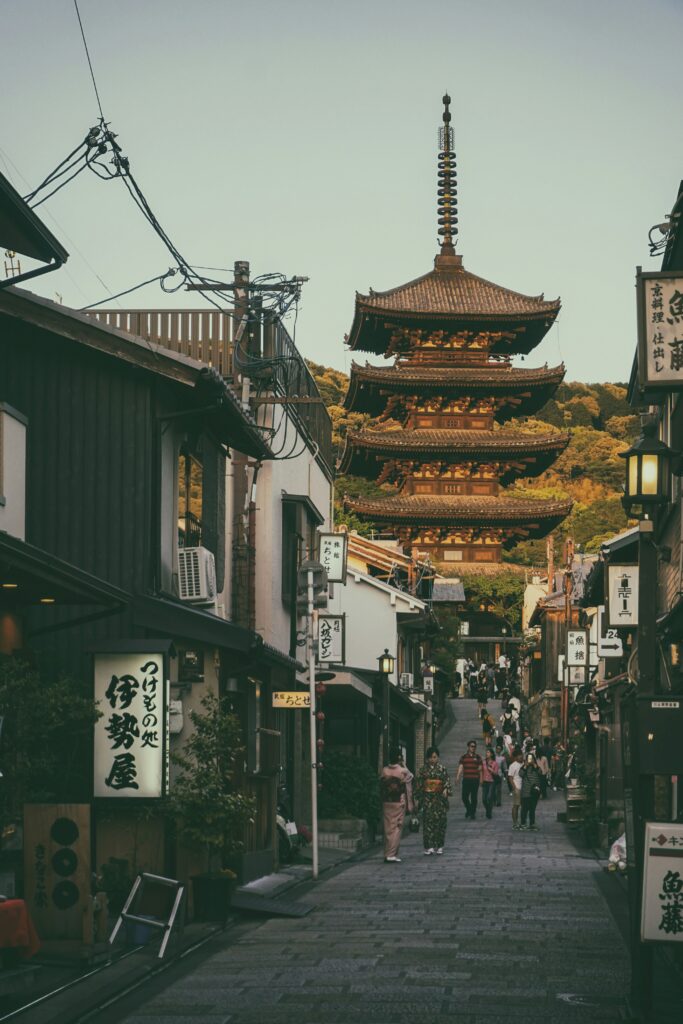 A street in Kyoto leading toward a traditional pagoda at sunset, with people walking along the shops.