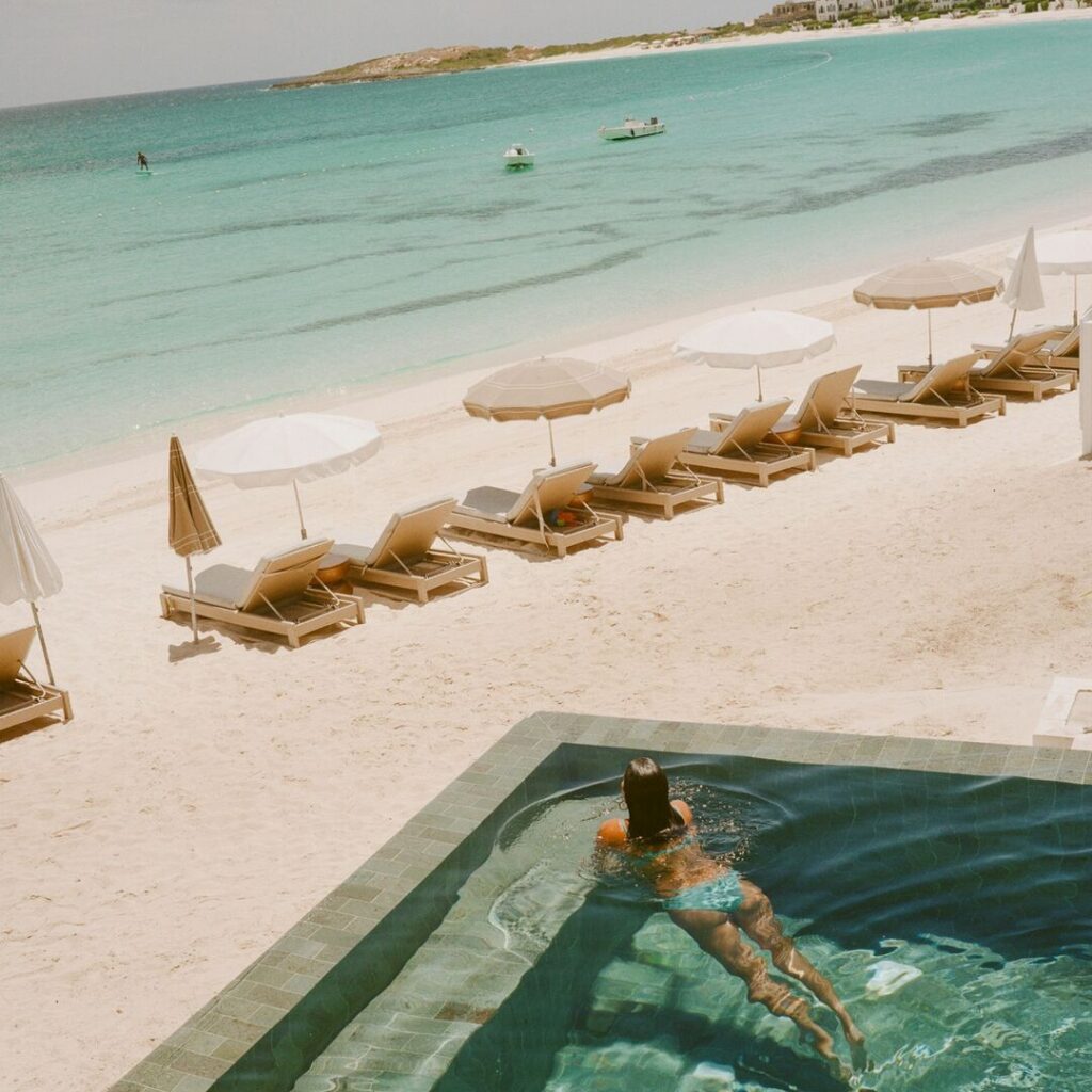 Woman relaxing in a private plunge pool overlooking a white-sand beach and turquoise water at Cap Juluca, Anguilla.