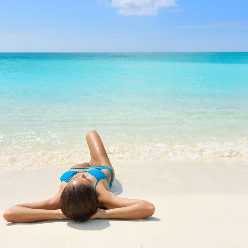 Woman relaxing on a white-sand beach during off-season Caribbean travel, with turquoise water and clear skies in the background.