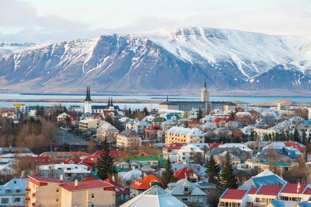 Panoramic view of Reykjavik, Iceland with snow-covered mountains in the background, colorful rooftops in the foreground.