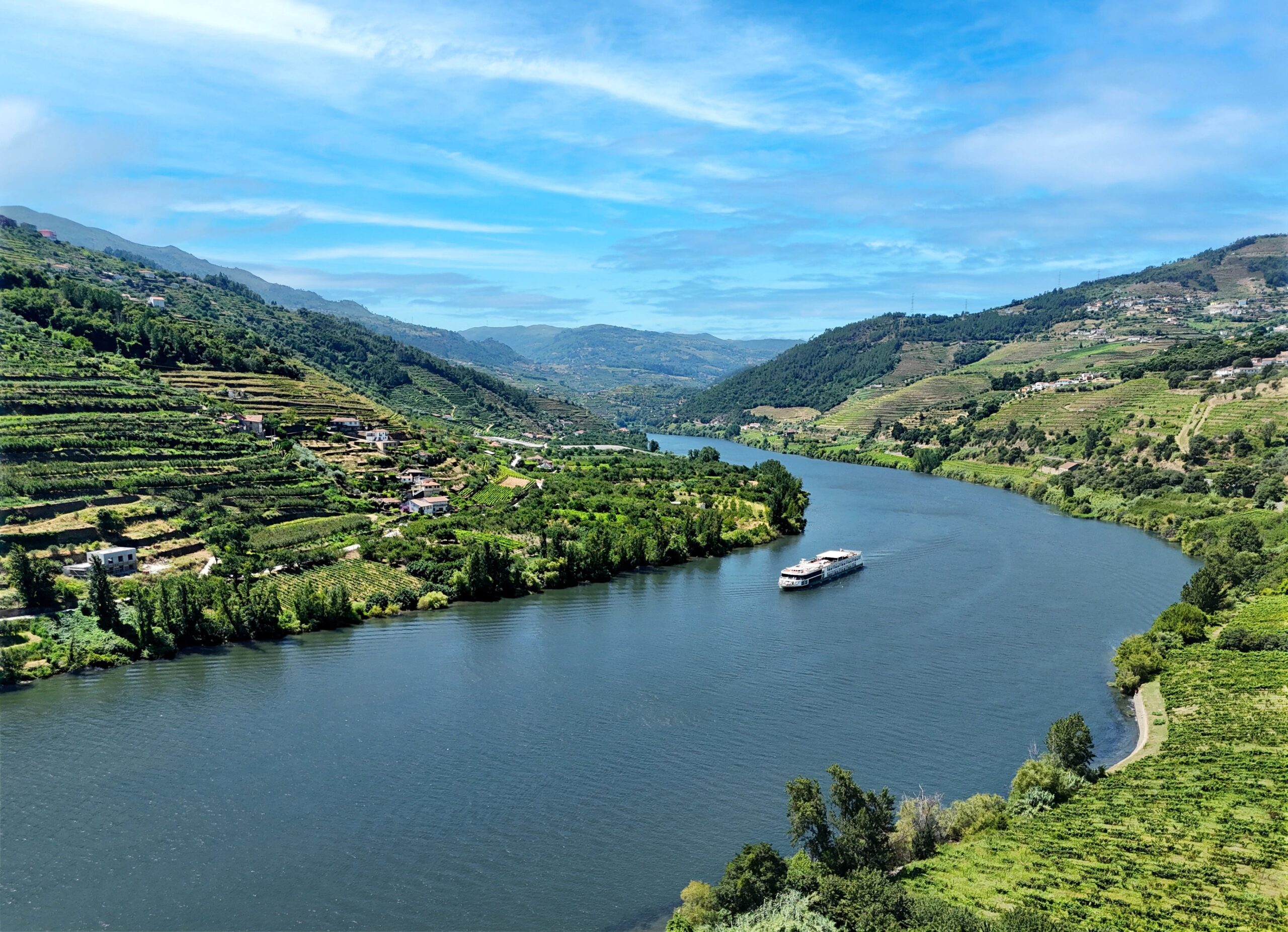 AmaWaterways’ AmaVida river ship sailing through Portugal’s Douro Valley, surrounded by terraced vineyards and rolling green hills.